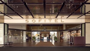 Una entrada de hotel moderna con fachada de vidrio, un cartel llamativo que dice 'SOFITEL' y un diseño interior limpio y minimalista.