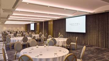 A conference room with round tables, chairs, and a projection screen displaying 'SOFITEL BRISBANE CENTRAL'.