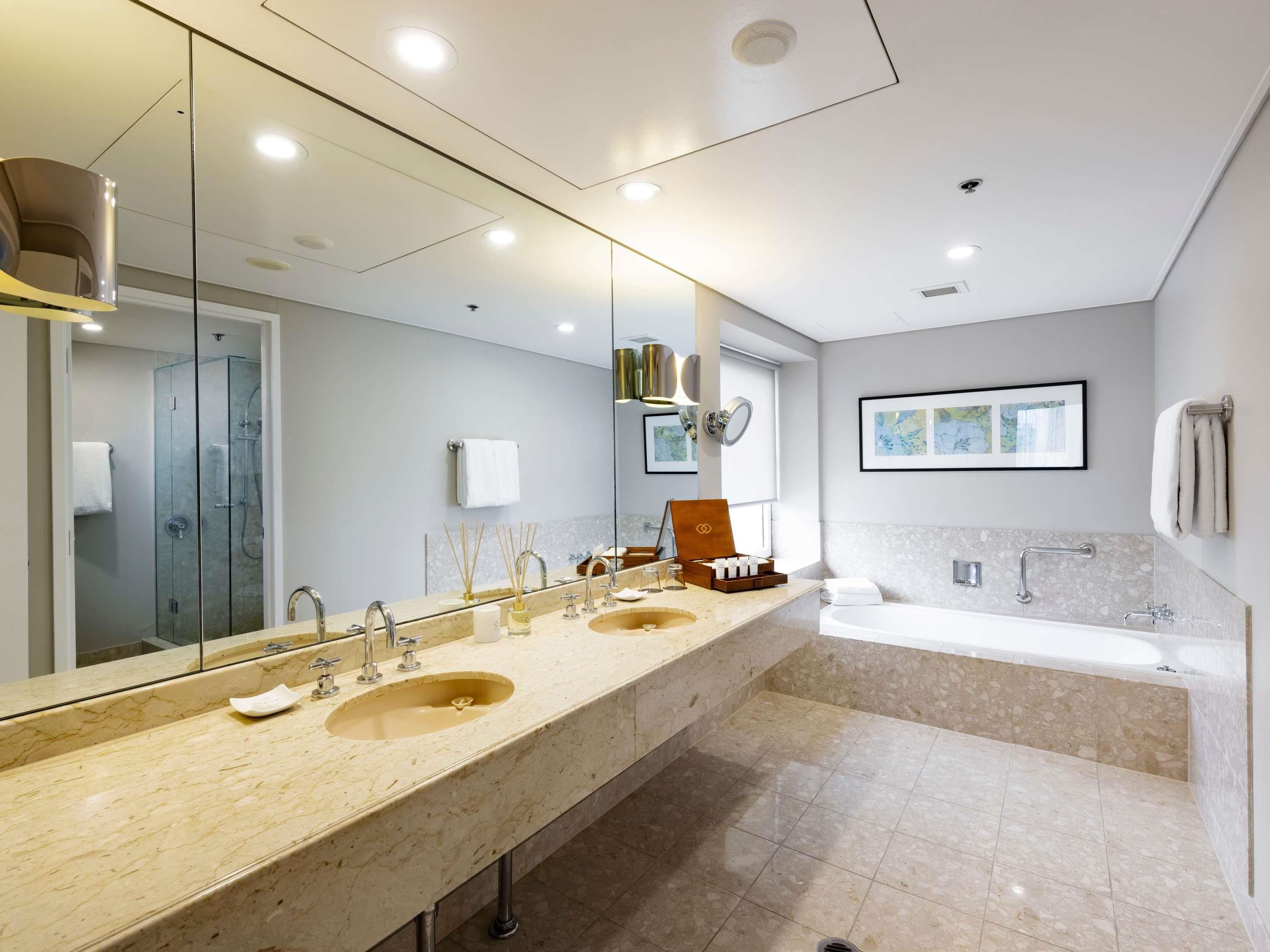 A modern bathroom with two sinks, a large mirror, a bathtub, and a shower enclosure.