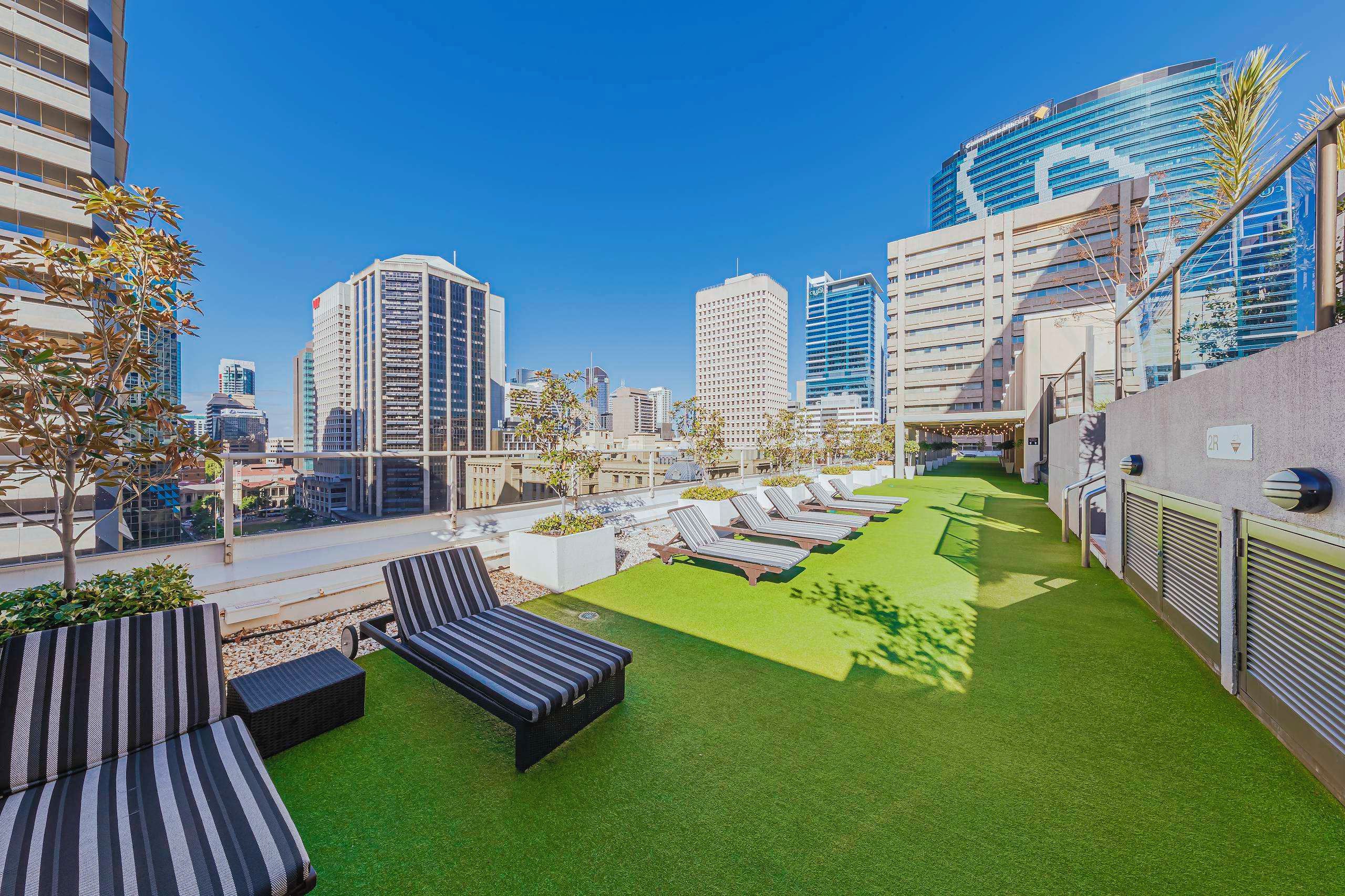 Une terrasse sur le toit, dotée d’un revêtement d’herbe artificielle, de chaises longues et offrant une vue sur les immeubles environnants.