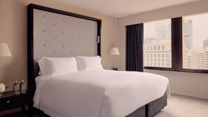 Habitación de hotel con una cama grande, una mesita de noche, una lámpara y vistas a la ciudad.