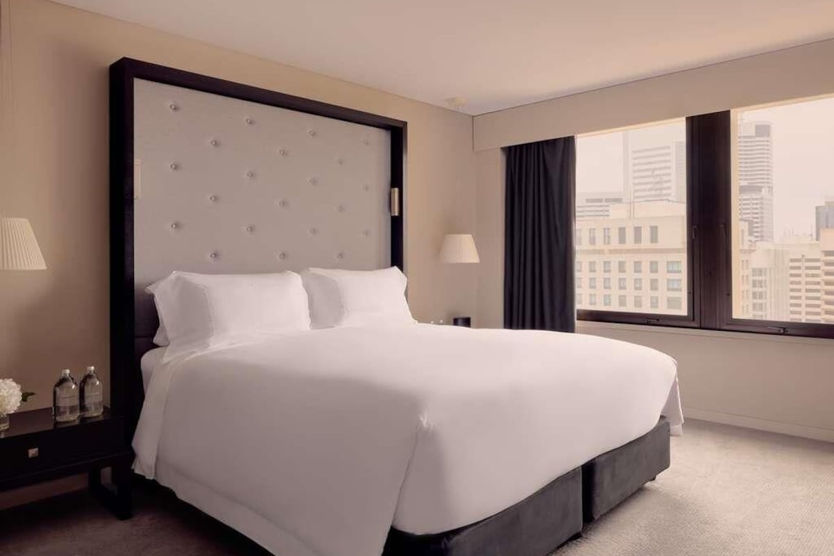 A hotel room with a large bed, a nightstand, a lamp, and a view of the city.