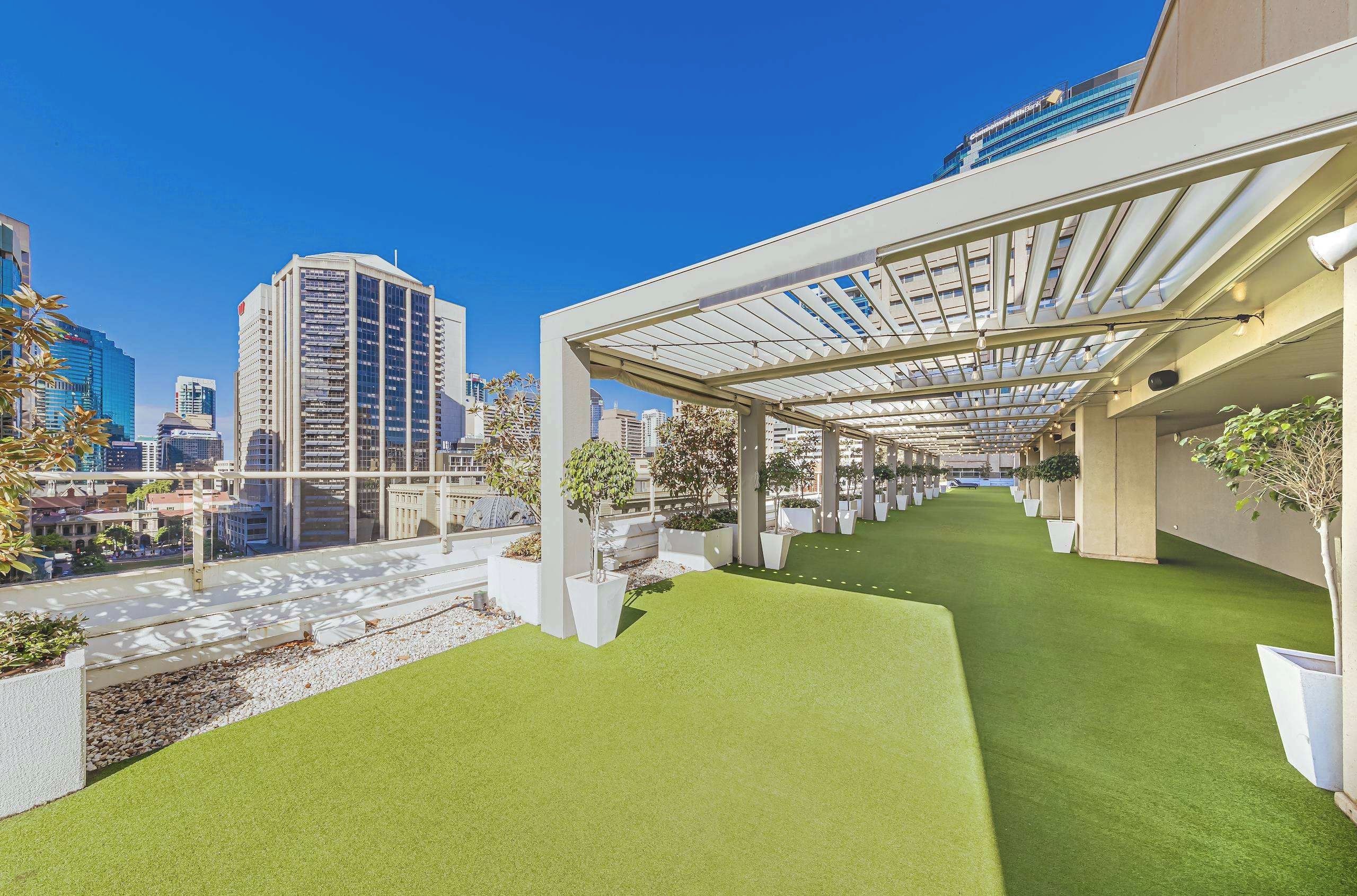 A rooftop garden with artificial grass, potted plants, and a pergola structure.