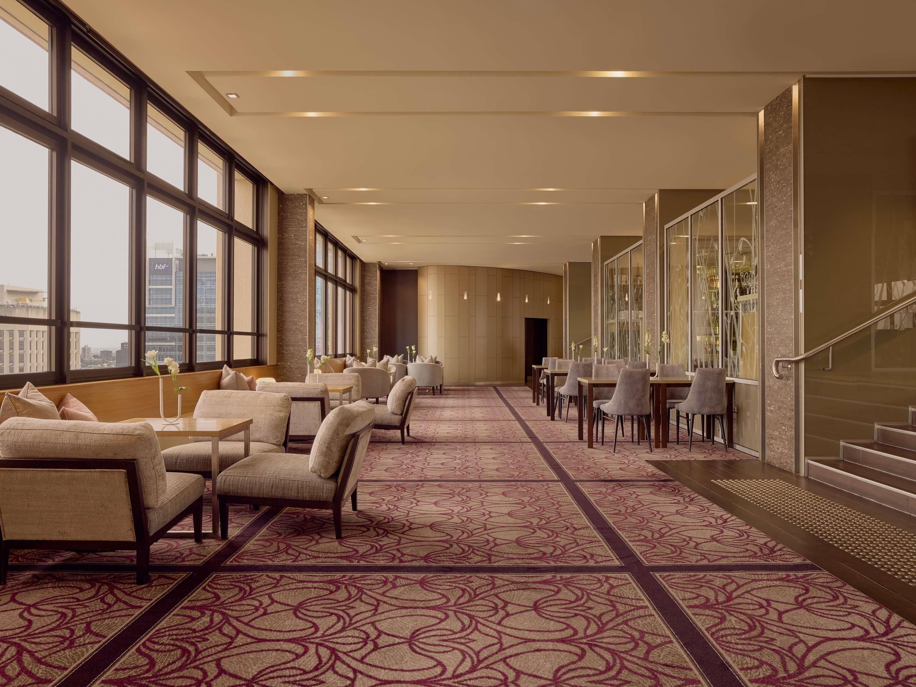 A hotel lobby with a long corridor, seating areas, and large windows offering city views.