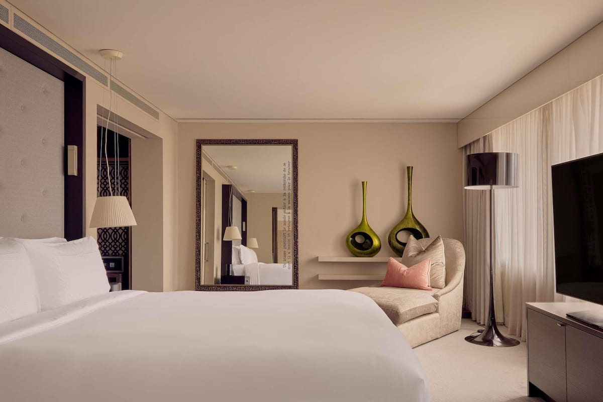 A hotel room with a large bed, a chair, a TV, and a mirror.