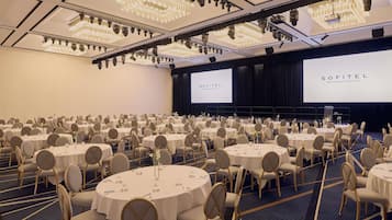 A conference room at Sofitel Brisbane Central with round tables, chairs, and a stage with a projection screen.