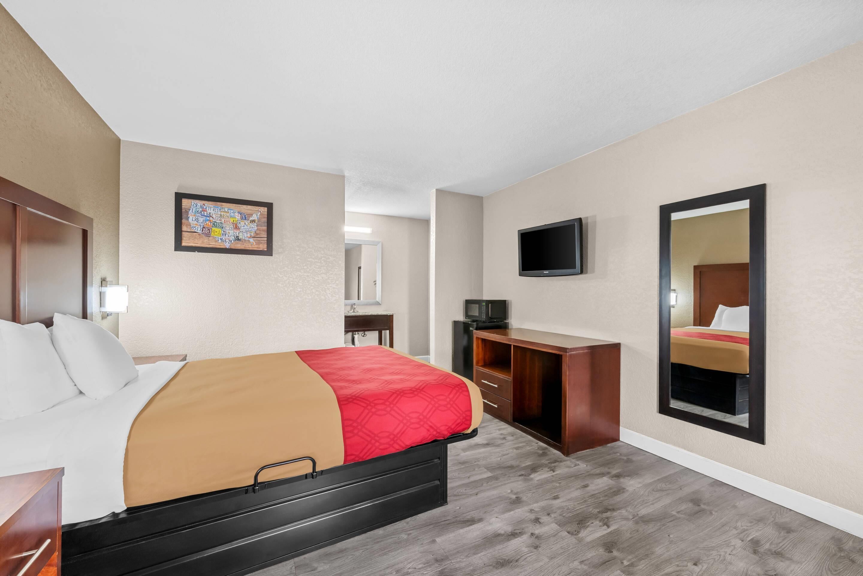 Una habitación de hotel con una cama, un escritorio, un televisor y un espejo.
