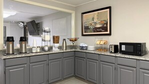 A modern kitchen with grey cabinets, a granite countertop, a coffee station, a microwave, and a framed artwork on the wall. - Econo Lodge Kannapolis - Concord (Kannapolis)