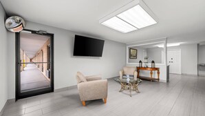 A modern living room with a flat-screen TV, a sofa, a coffee table, and a door leading to a hallway. - Econo Lodge Kannapolis - Concord (Kannapolis)