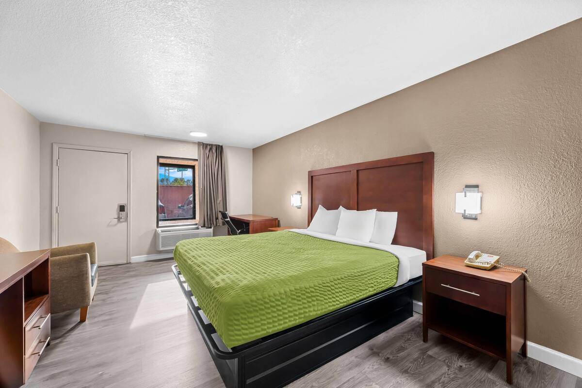 A hotel room with a bed, bedside table, and a desk.