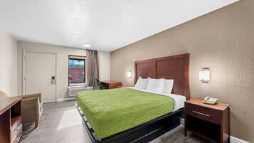 Habitación de hotel con cama, mesita de noche, lámpara y vista al exterior.