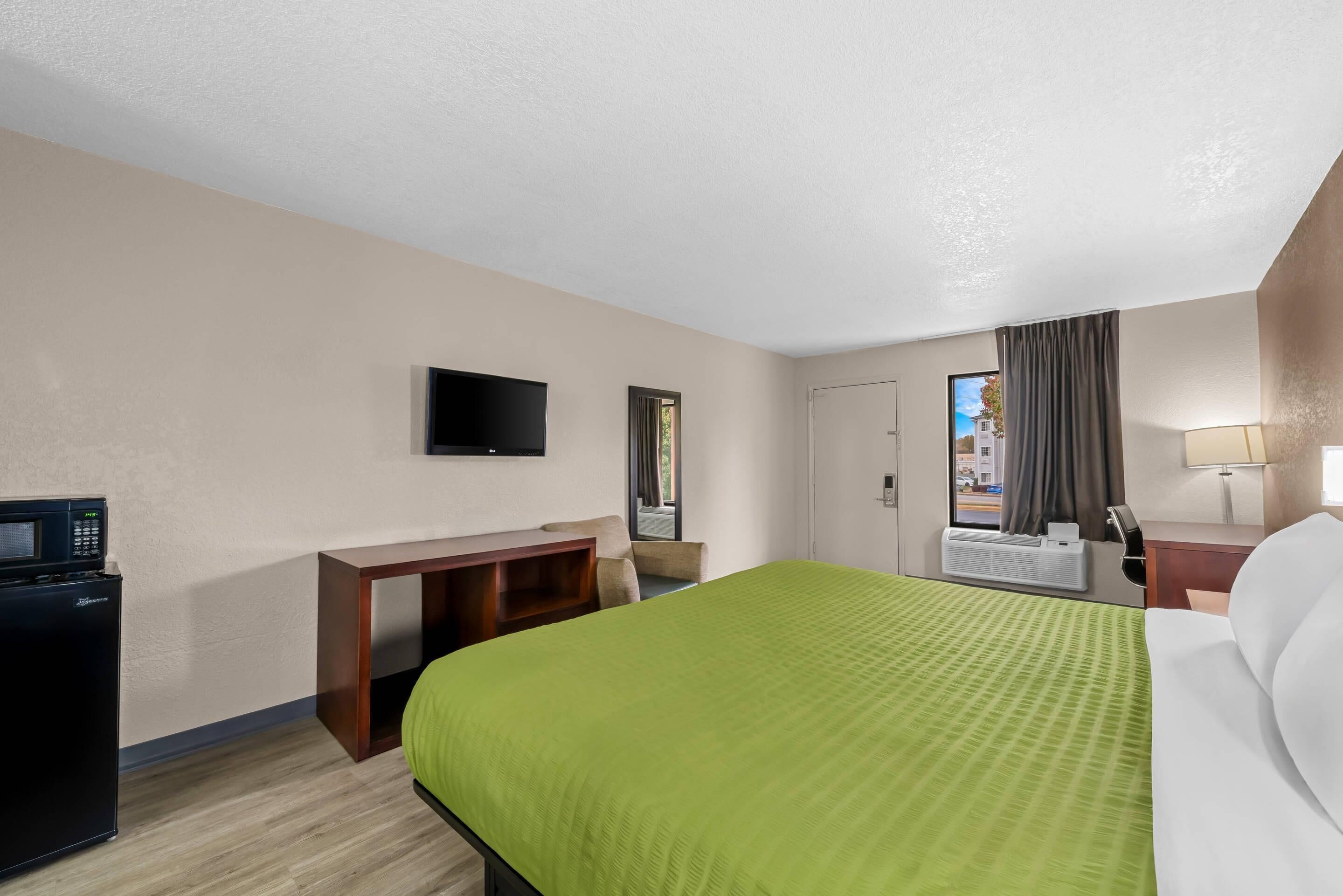 A hotel room with a bed, a desk, a television, and a window with curtains.