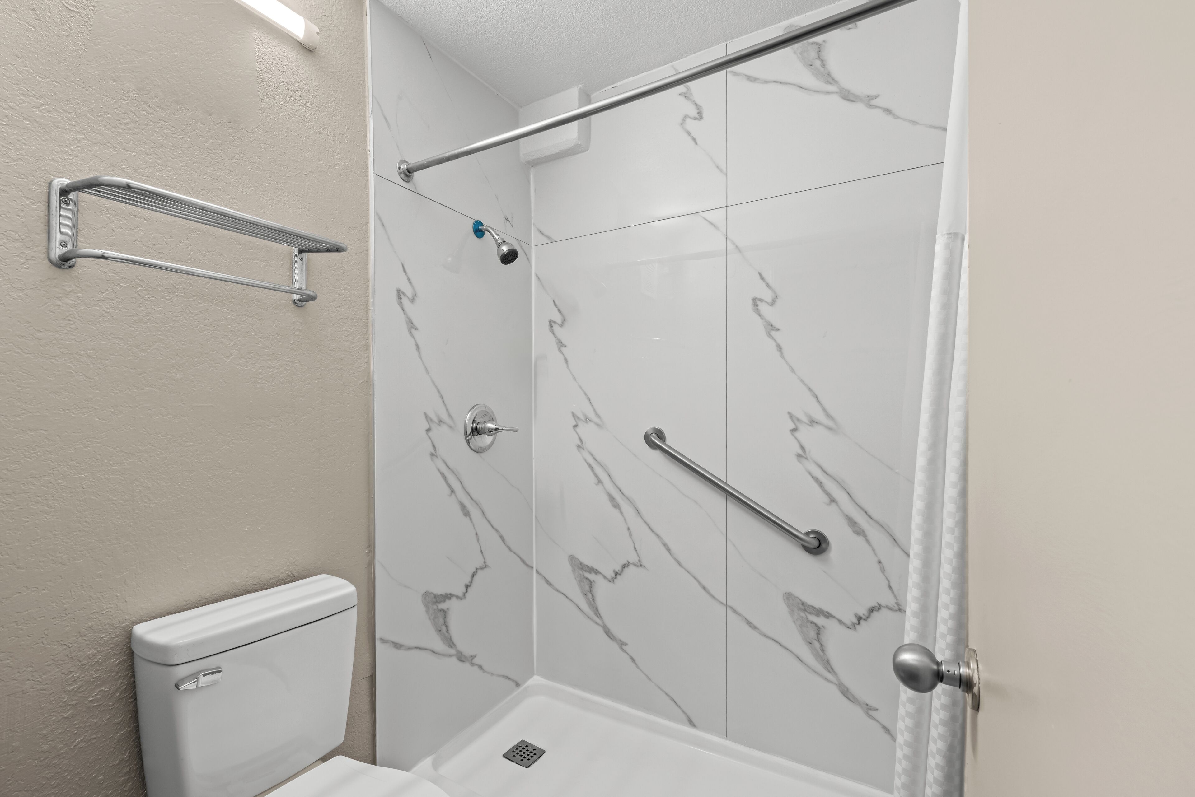 Een douche met een glazen deur, een handgreep en een toilet met een witte tank.