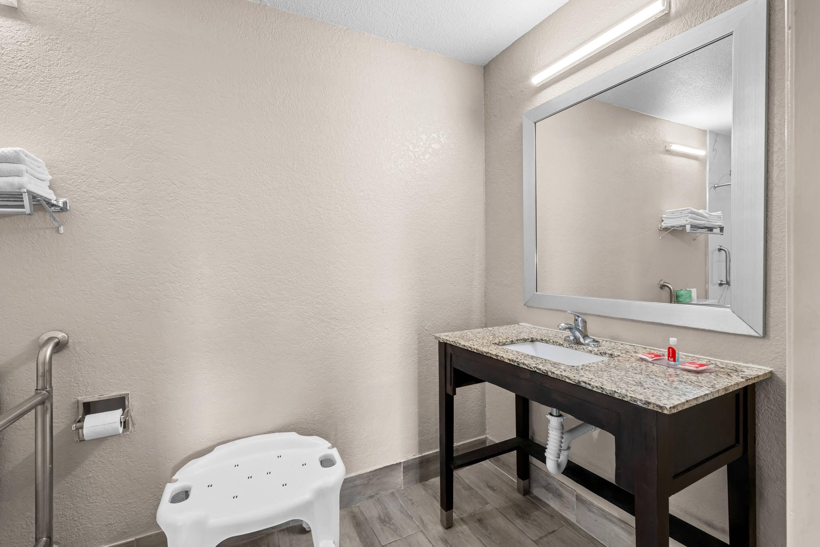 Baño con lavamanos, espejo, toallero y un taburete blanco.