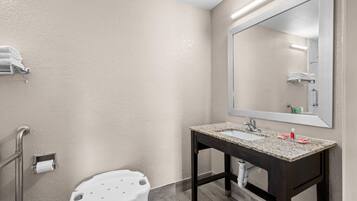 Baño con lavamanos, espejo, toallero y un taburete blanco.