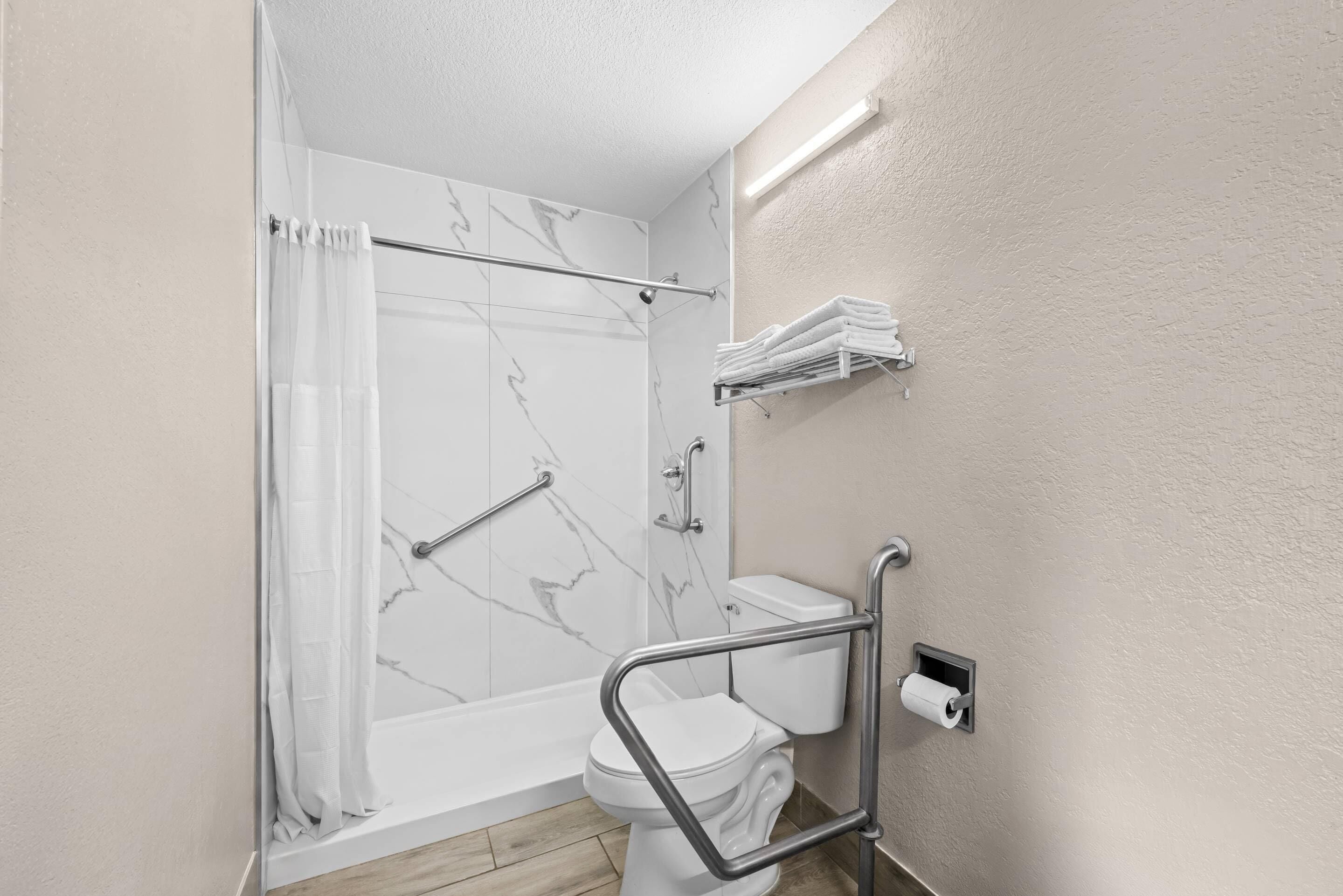 Ein Badezimmer mit Dusche, Toilette und Haltegriffen.