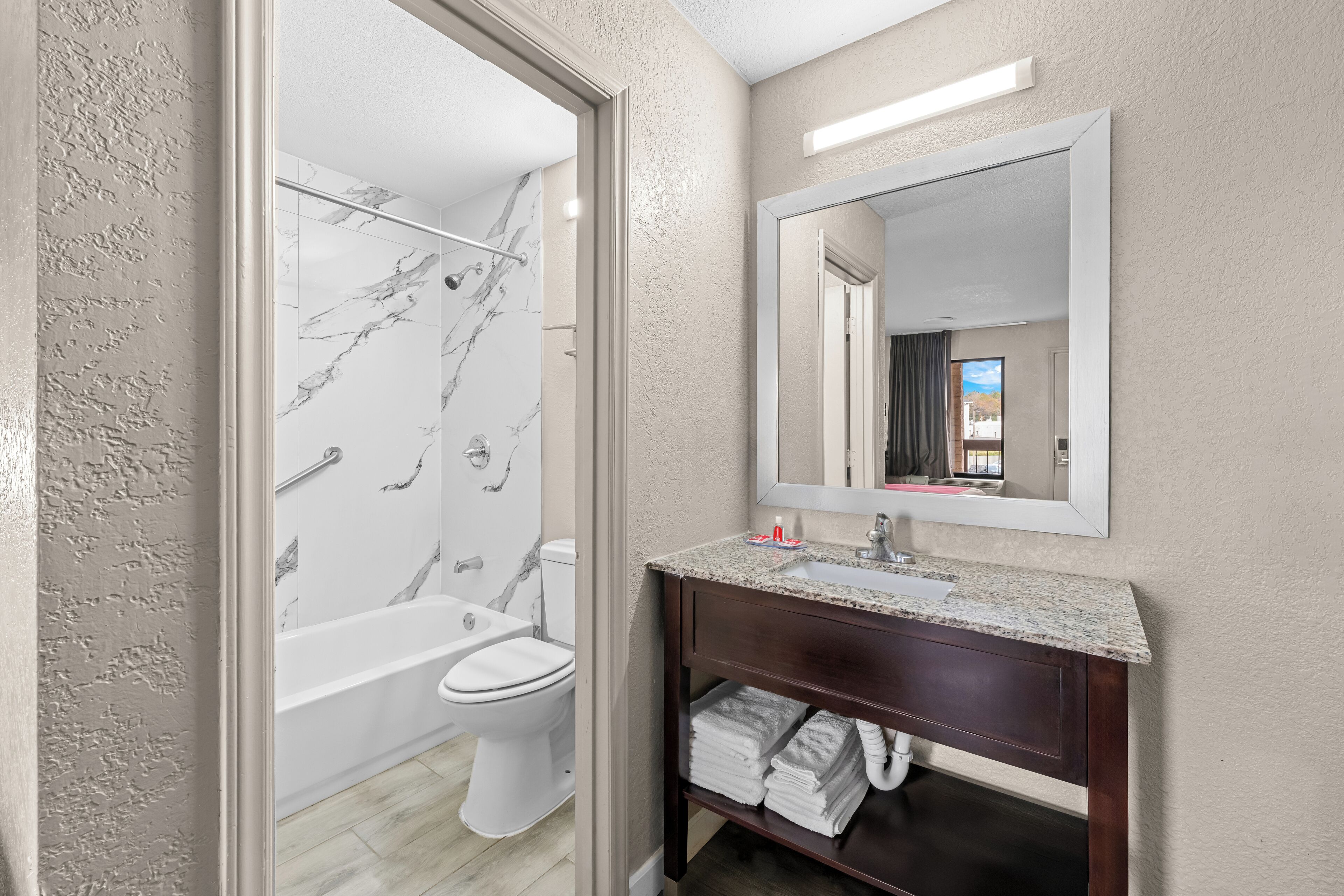 A modern bathroom with a marble shower, a toilet, and a vanity with a mirror.