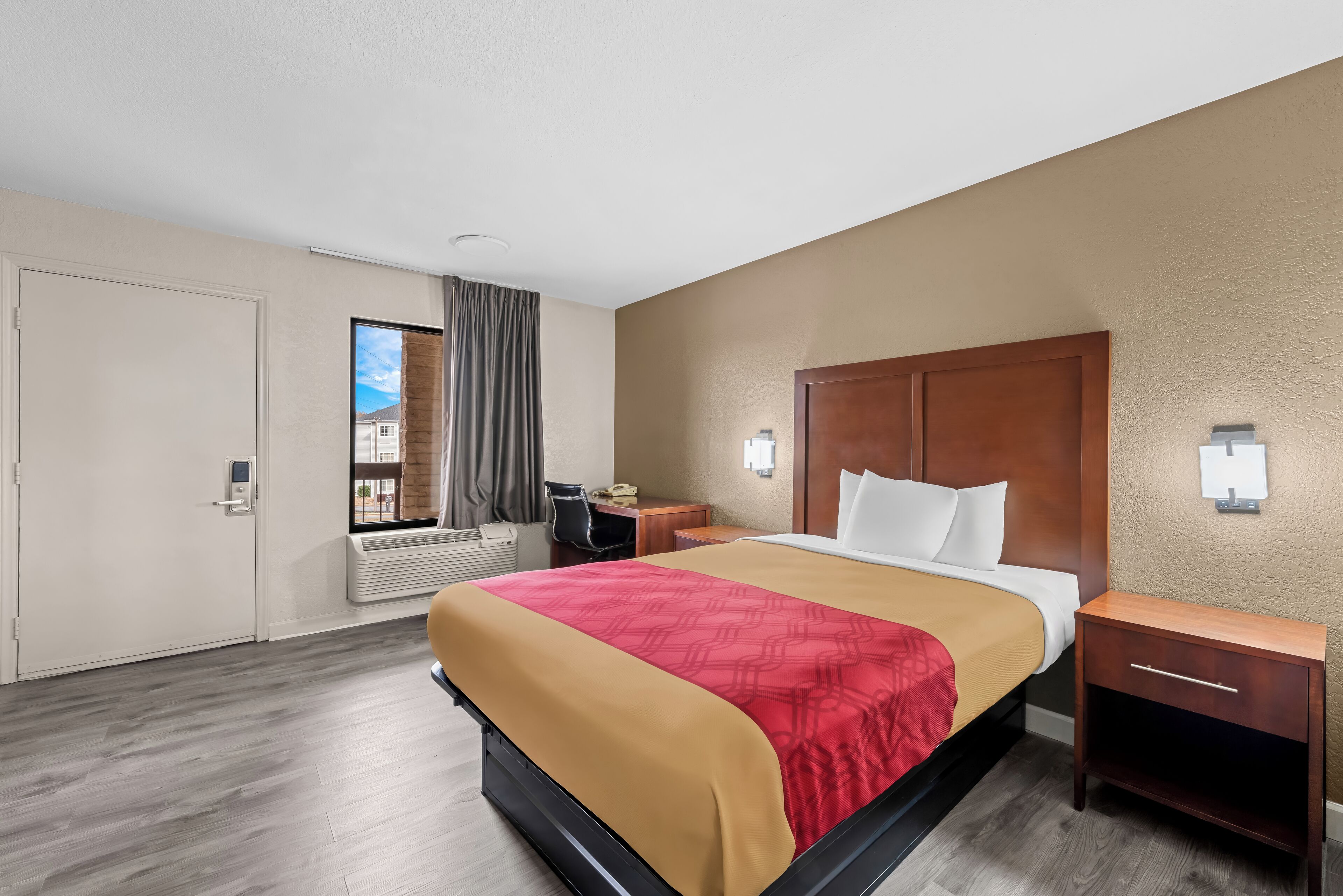 Habitación de hotel con cama, escritorio, silla y ventana con cortinas.
