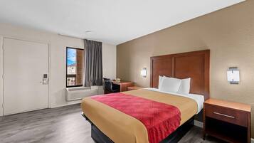 Una habitación de hotel con una cama, mesitas de noche, un escritorio y una ventana con cortinas.