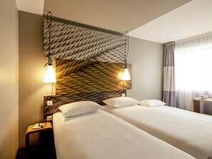 Una habitación de hotel con una cama grande, dos lámparas de noche, una mesita de noche y una ventana con cortinas.