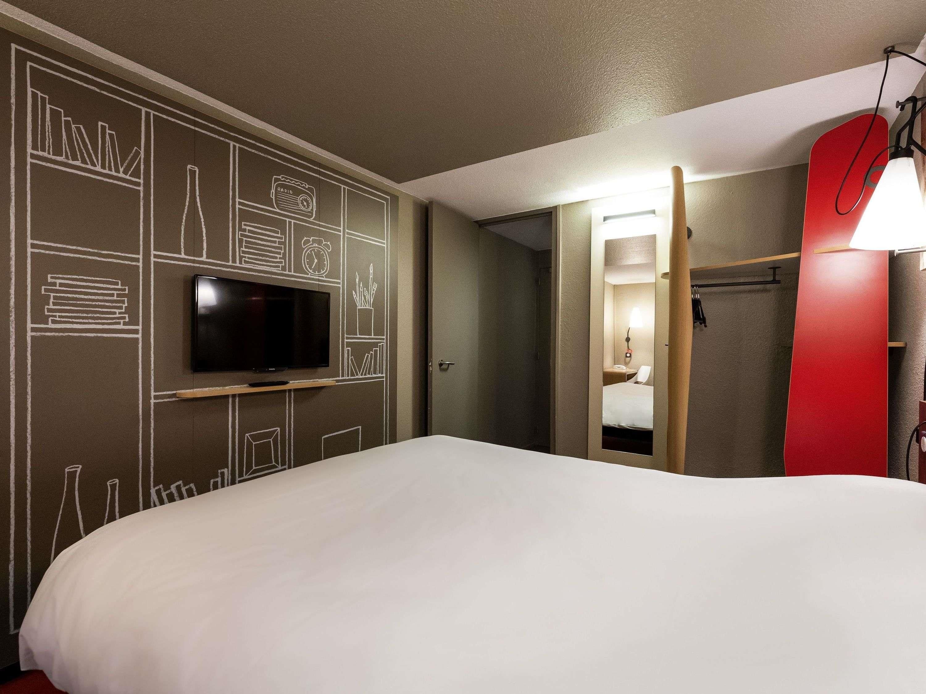 Quarto de hotel com uma cama, uma TV fixada na parede e um prancha de surf vermelha.