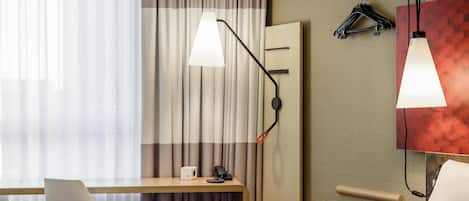 A hotel room with a desk, chair, bed, and two pendant lights.