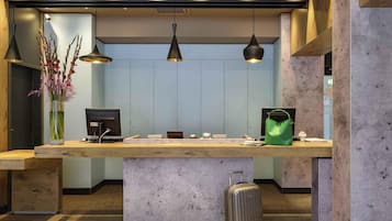 A reception desk with a computer, a green bag, and a suitcase.