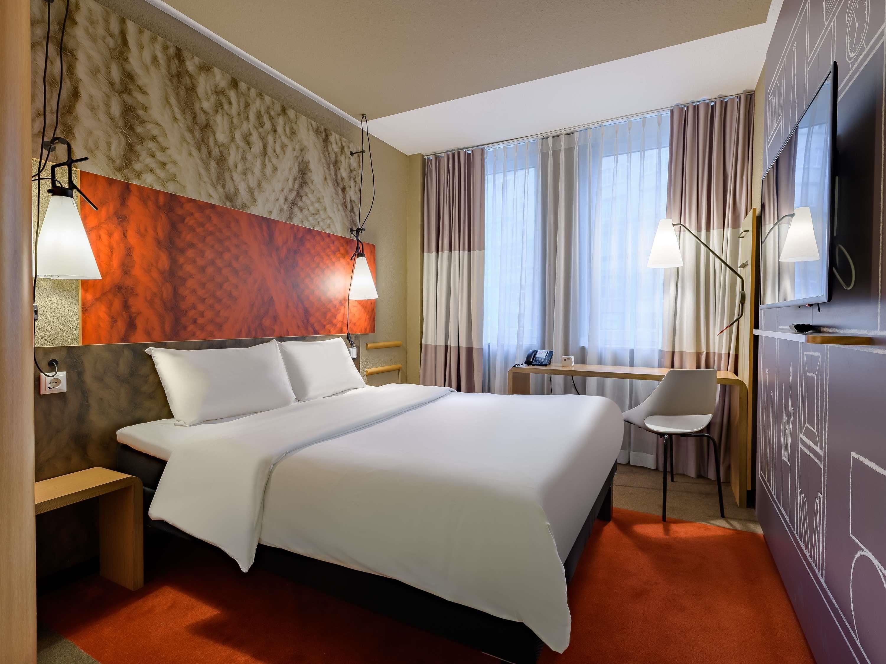 Ein Hotelzimmer mit Bett, Nachttisch, Schreibtisch, Stuhl und Fernseher.