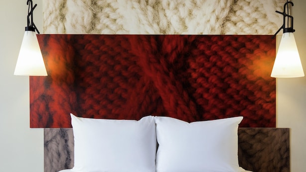 A bed with white linens, a red textured wall behind it, and two wall-mounted lamps. - ibis Hotel Köln Am Dom (Cologne)