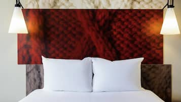 Un lit avec du linge de lit blanc, un mur rouge à texture derrière, et deux lampes fixées au mur.