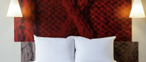 Una cama con sábanas blancas, una pared texturizada de color rojo y dos lámparas fijadas a la pared.