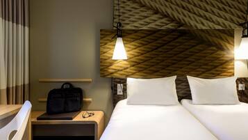 Een hotelkamer met twee bedden, een bureau, een stoel, een nachtkastje en een hoofdbord met een structuur.