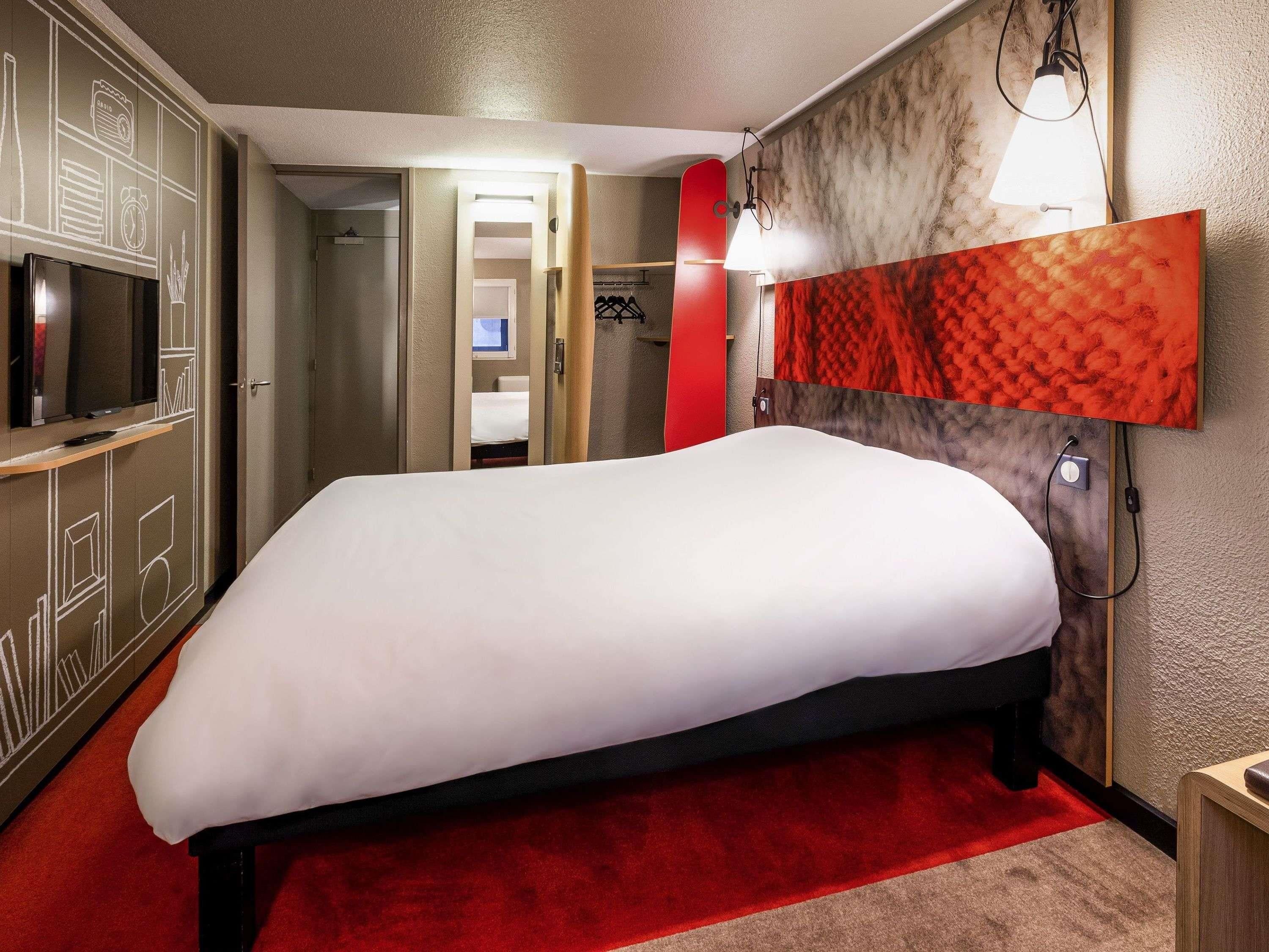 Una camera d'albergo con un letto, una televisione, una parete decorata di rosso e un tappeto rosso.