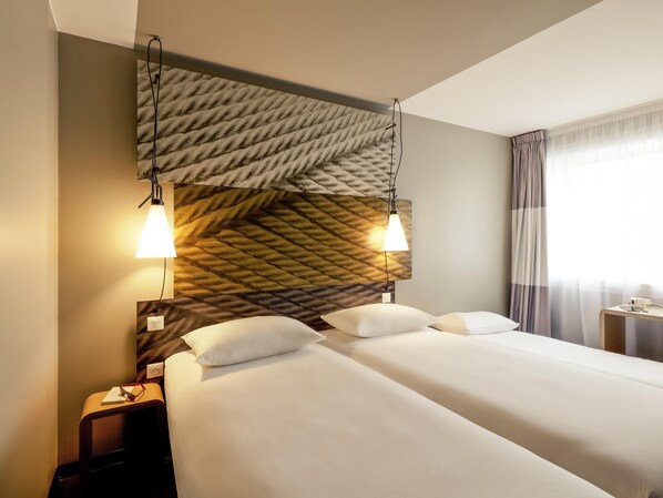 A hotel room with a large bed, two bedside lamps, a nightstand, and a window with curtains. - ibis Hotel Köln Am Dom (Cologne)