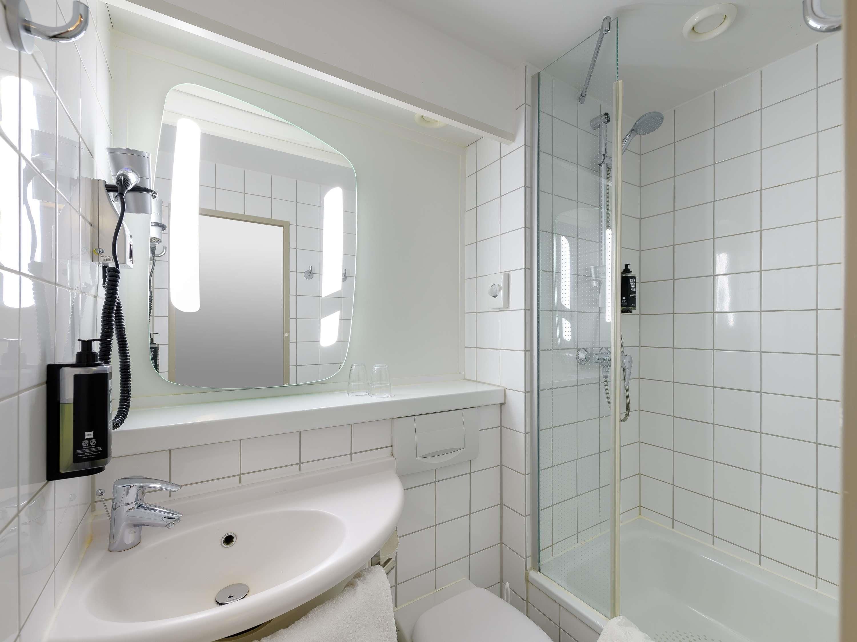 Un baño moderno con lavamanos blanco, espejo, ducha con mampara de vidrio y retrete.