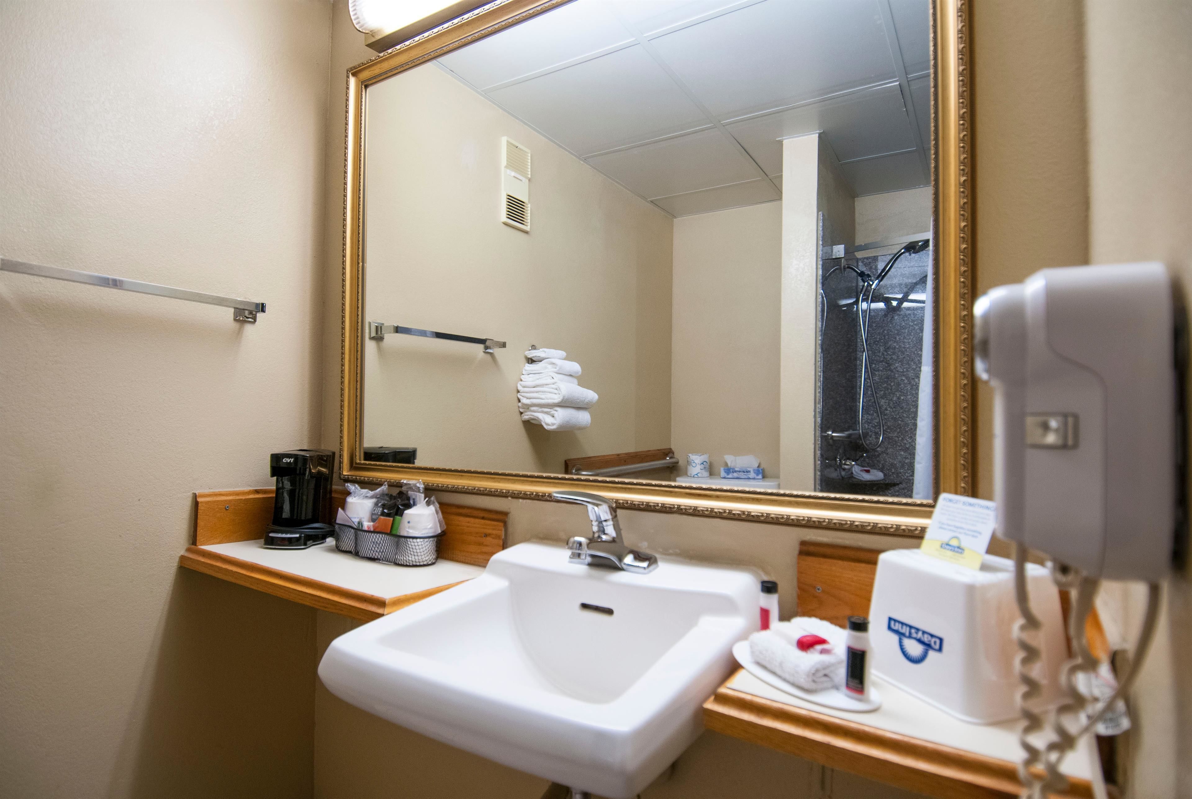 A hotel bathroom with a sink, mirror, towel rack, and a hairdryer.