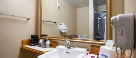 Un baño de hotel con lavamanos, espejo, toallero y secador de pelo.