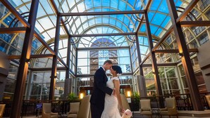 Una pareja besándose en un amplio atrio con techo de vidrio y muebles modernos.
