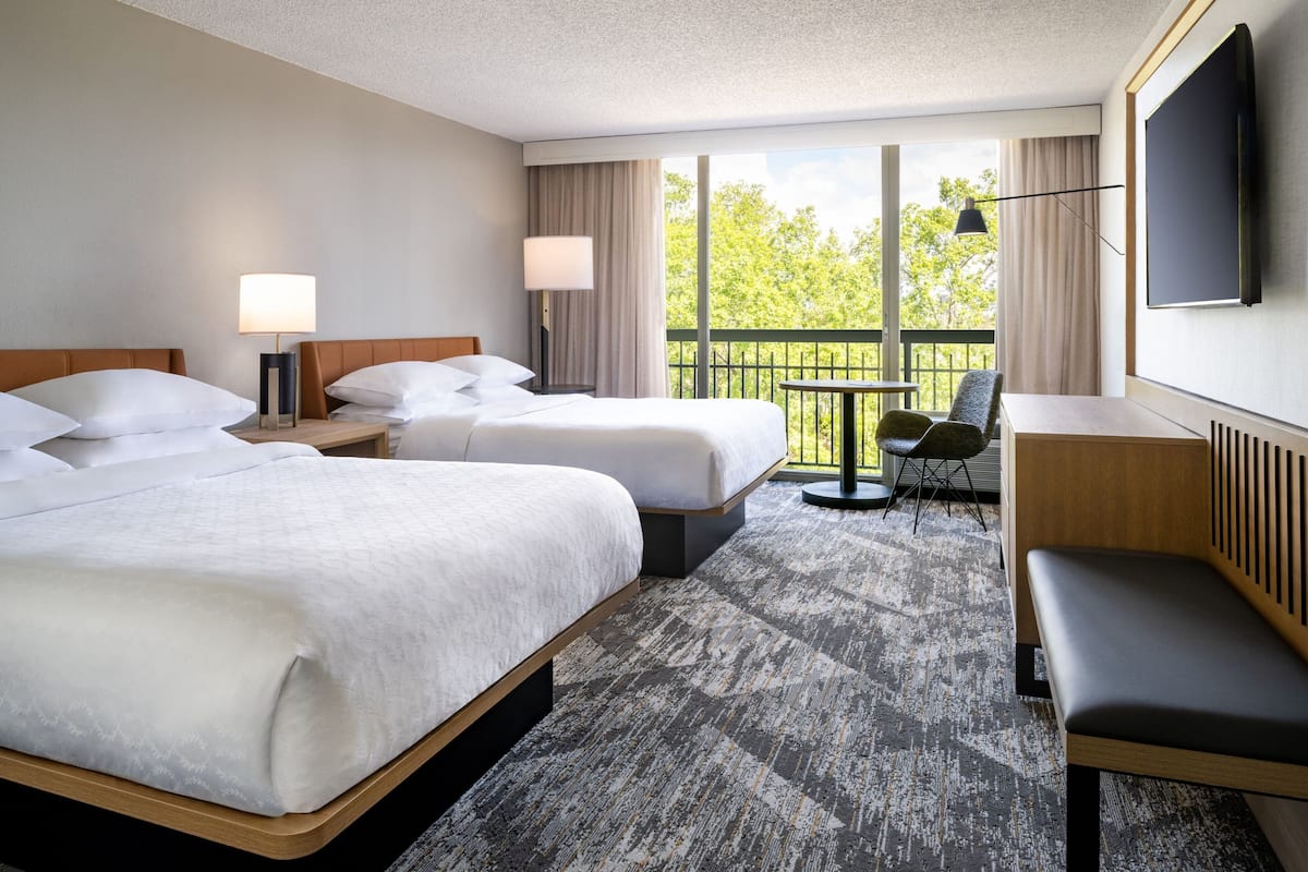 A hotel room with two beds, a desk, a chair, and a TV.