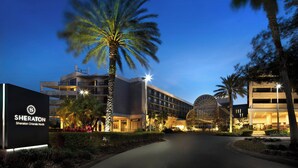 Un hotel Sheraton Orlando North de diseño moderno, con una palmera grande, entrada bien iluminada y cielo despejado.