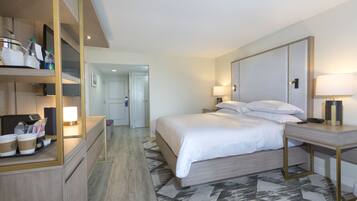 A hotel room with a bed, bedside tables, a desk with a lamp, a mirror, and a coffee station.