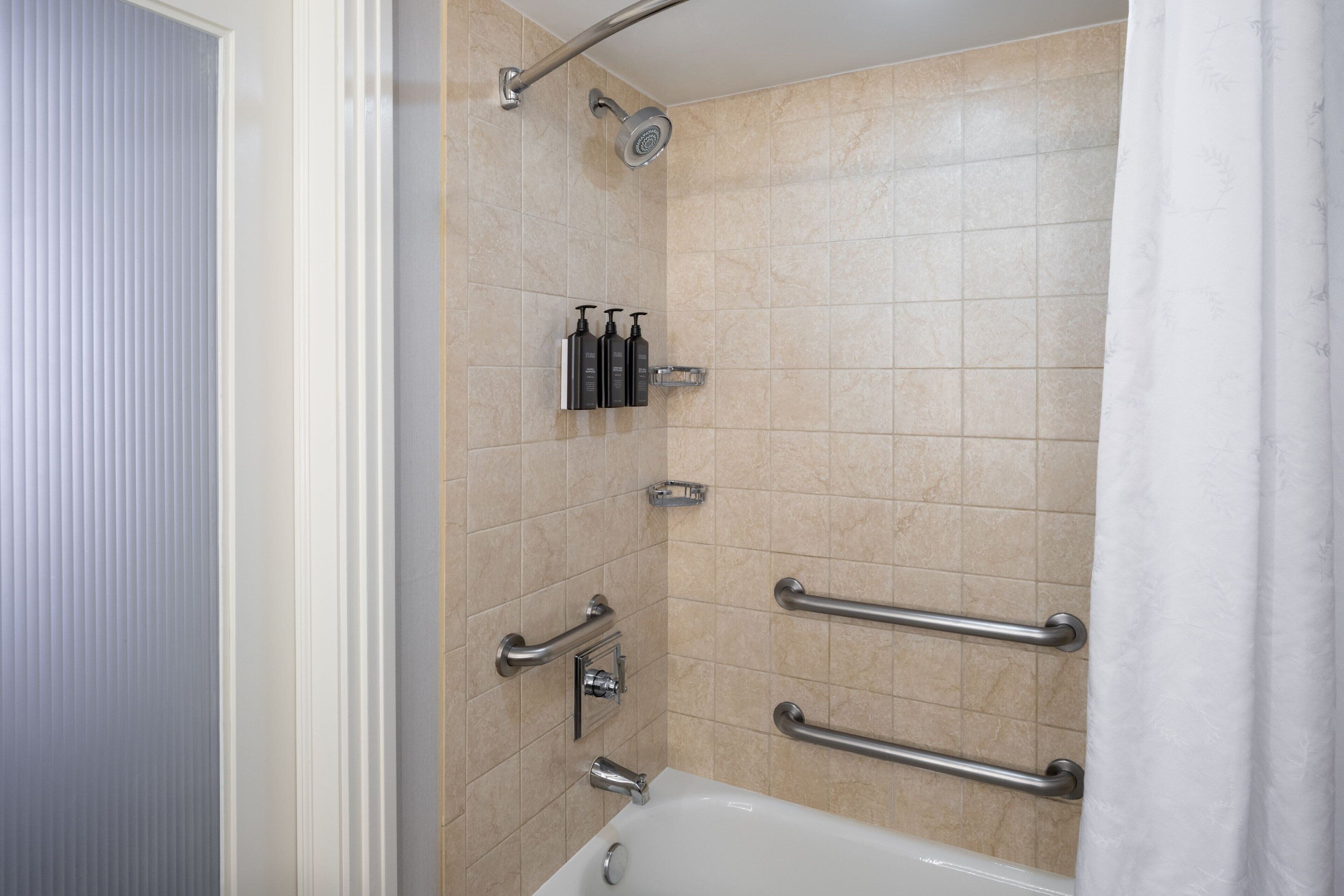 Un baño con bañera, ducha con cabezal de ducha móvil y barras de apoyo.