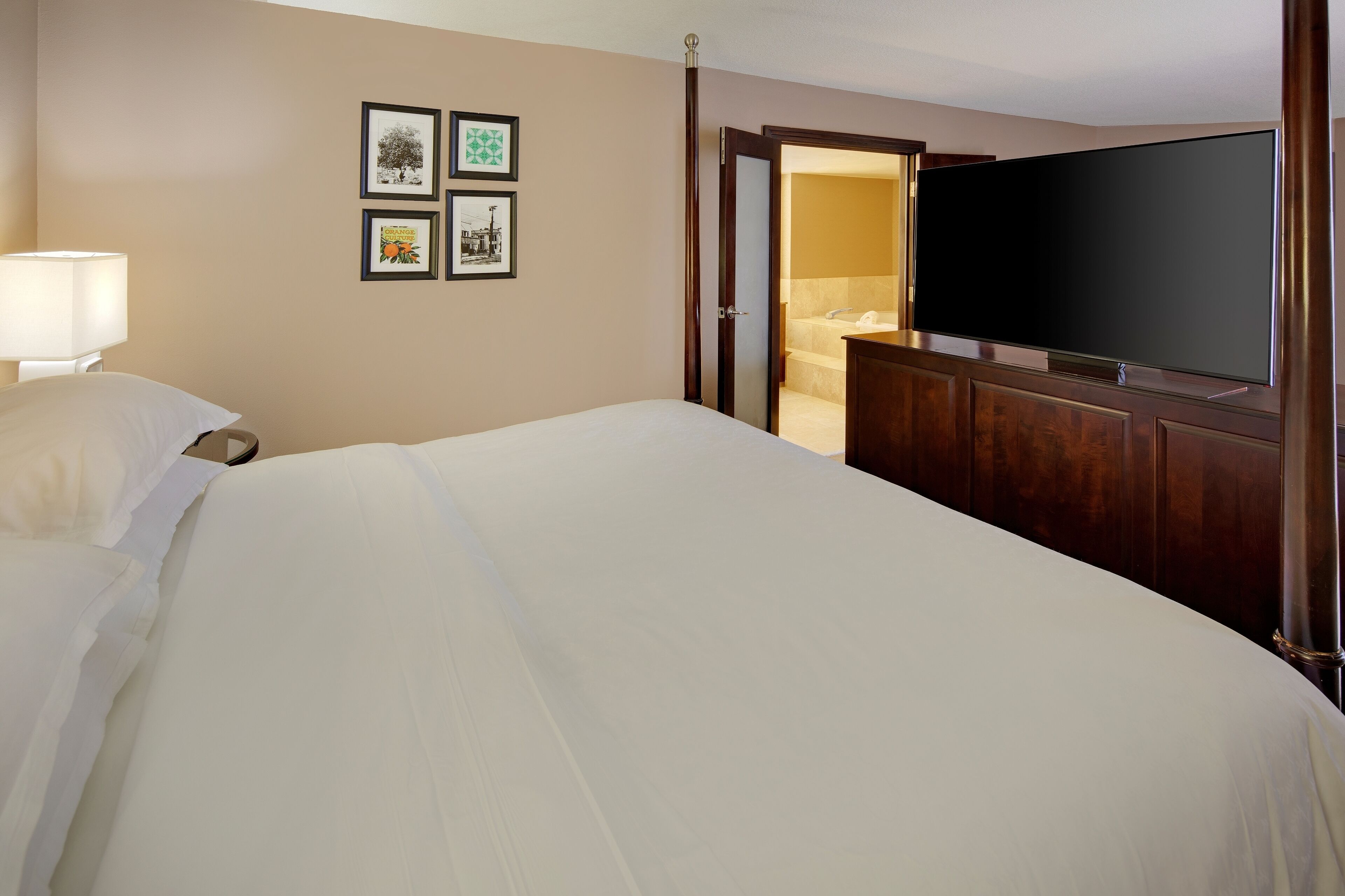 A hotel room with a large bed, a television, and framed pictures on the wall.