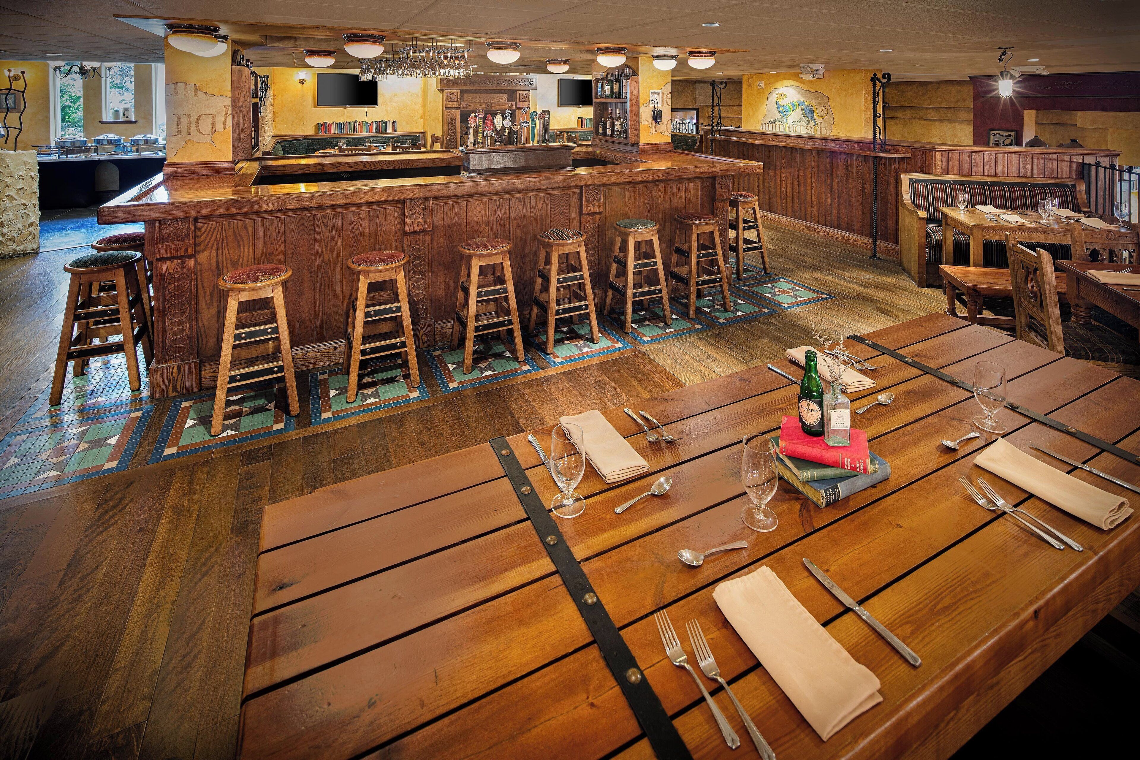 A bar area with wooden stools, a bar counter, and a dining area with tables set for two.