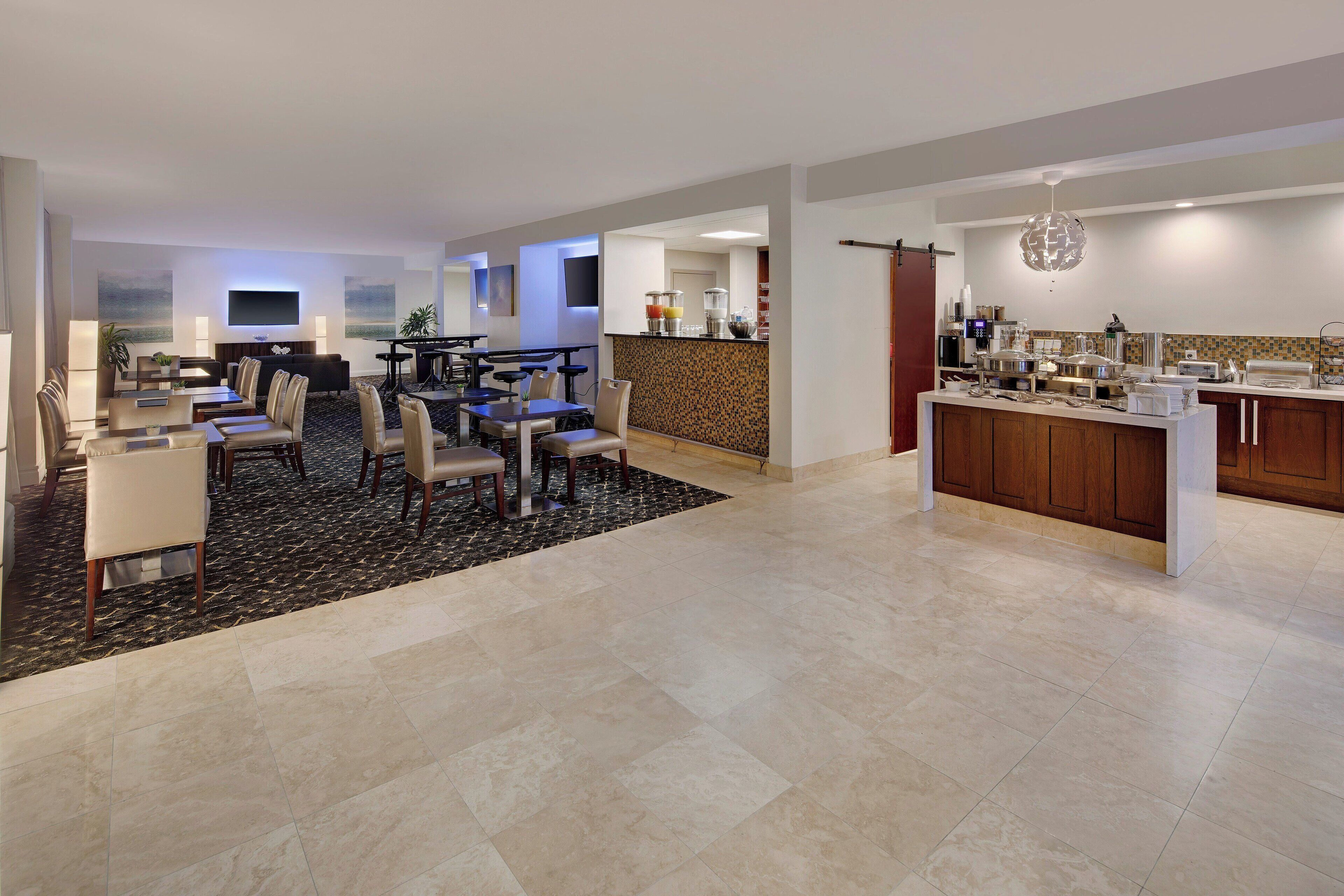 A modern hotel lobby with a dining area, a kitchen, and a bar.