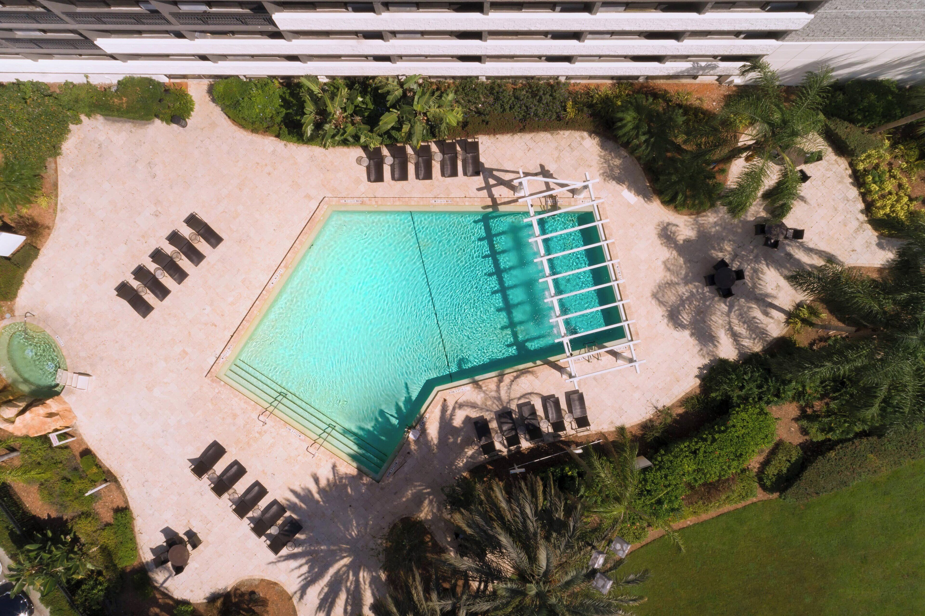 An aerial view of a pool area with sun loungers, a pool, and surrounding greenery.