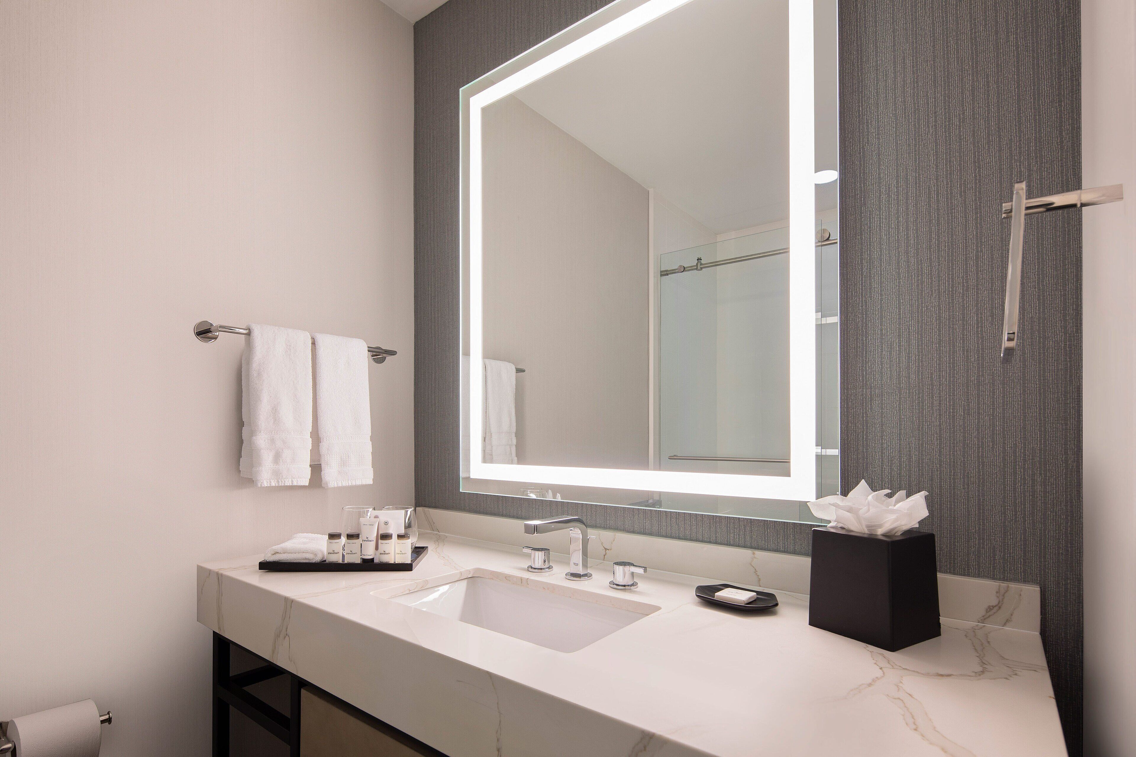A modern bathroom with a large mirror, a white sink, and a towel rack.