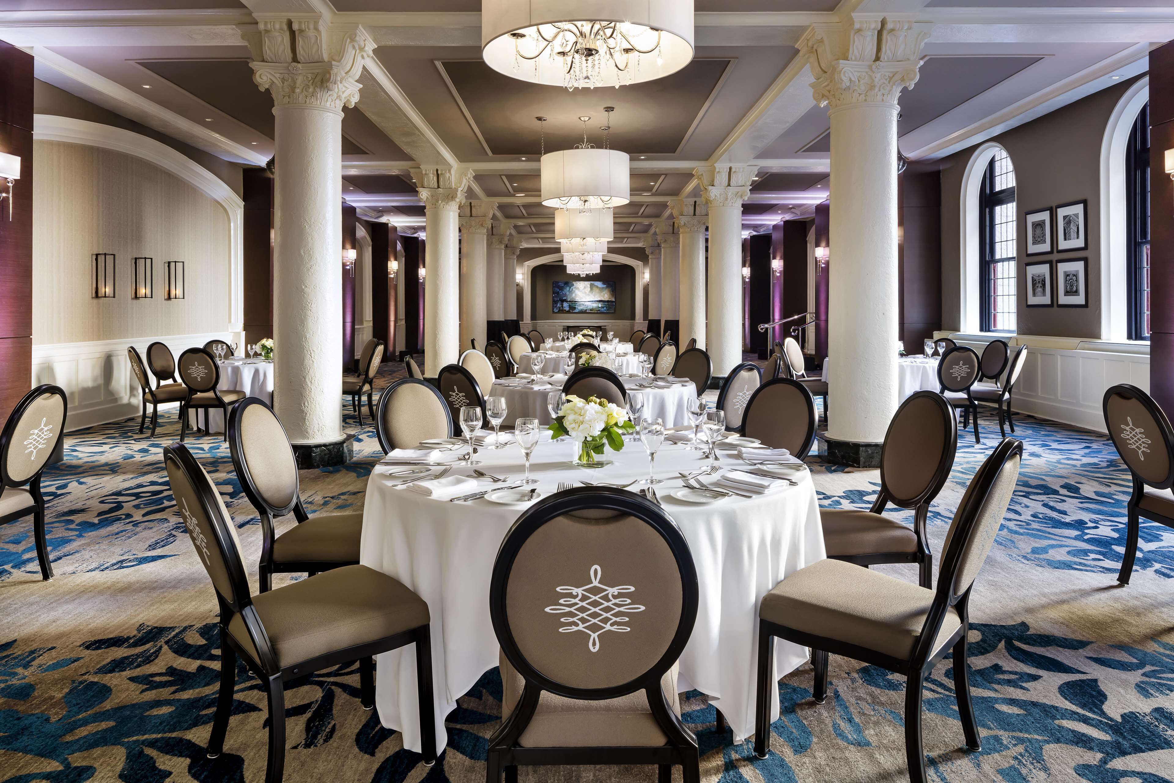 A formal dining room with round tables, chairs, and chandeliers.