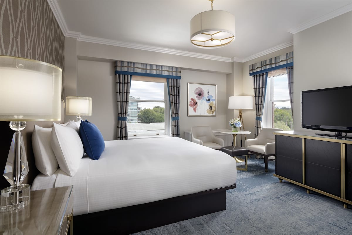 A hotel room with a large bed, a desk, a television, and a view of the city.