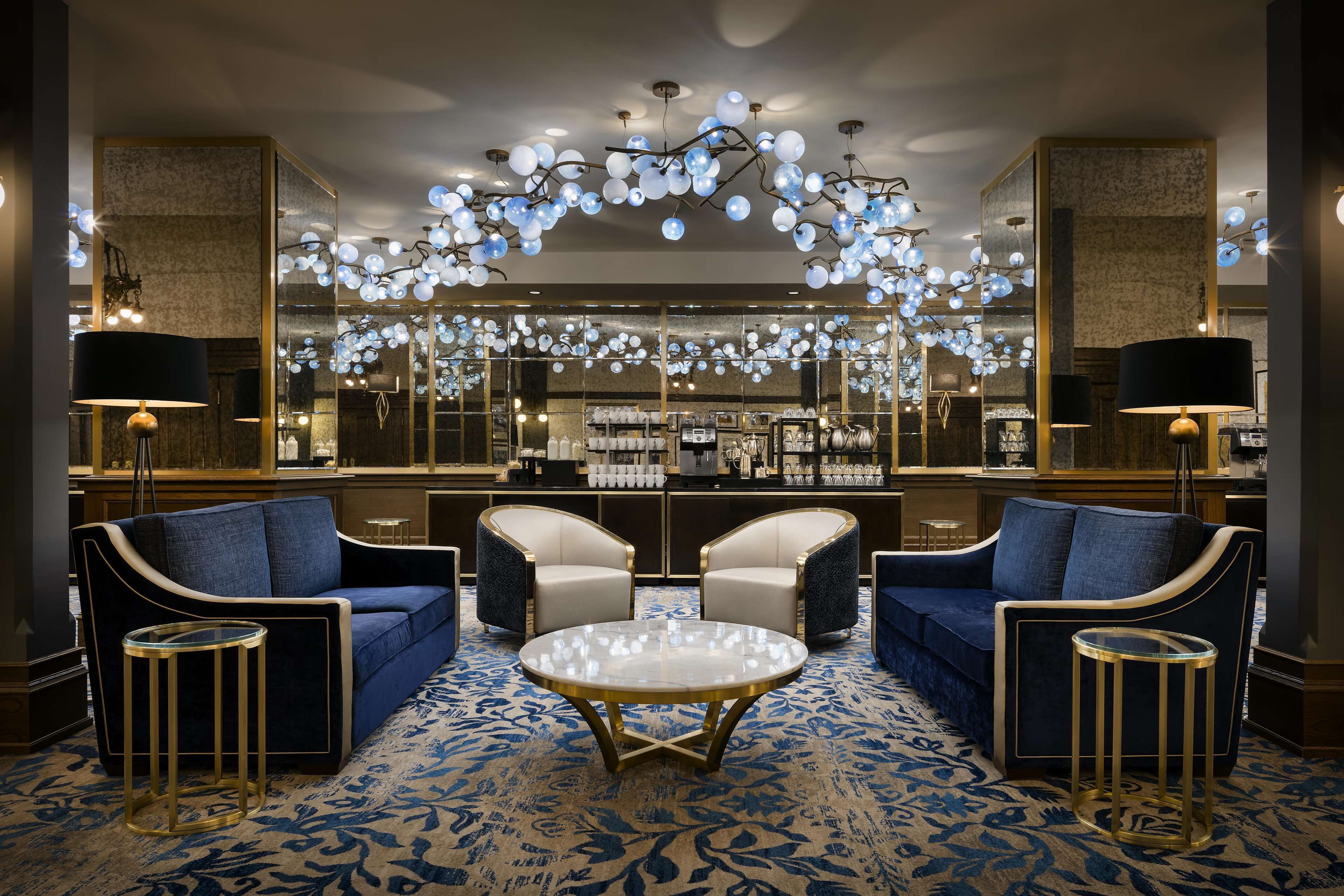 A luxurious lobby with a blue sofa set, a round coffee table, and a bar area in the background.